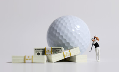 A bunch of $100 bills and a miniature golfer in front of a white golf ball.