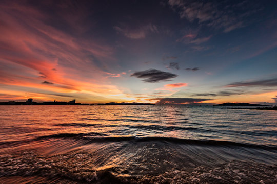 Sunset at the beach of Kota Kinabalu, Borneo. Tilt shift photography of the falling sun at the shore of Sabah, Malaysia. Colorful red and yellow sky with some clouds and small waves at the beach