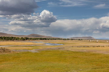 Clouds over the steppe of Mongolia. Endless horizon. The beautiful landscape of Mongolia near the city of Karakorum. Cows graze in background