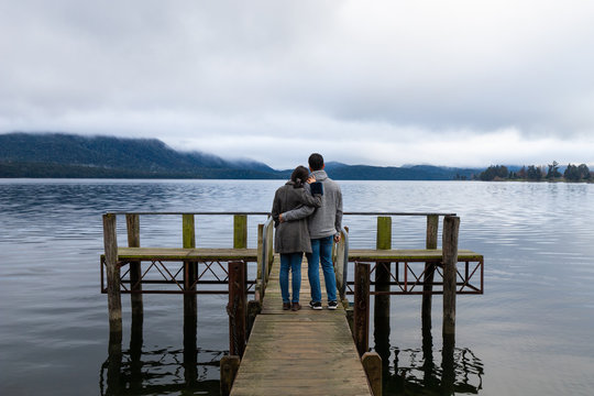 Young Asian couple hugging leaning on shoulder on the bridge Lake Te Anau New Zealand