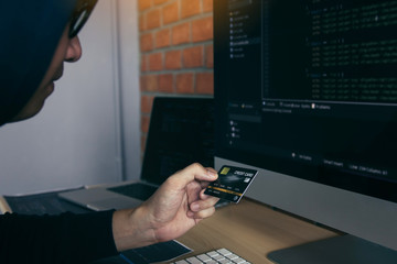 Hacker in the hood working with computer and holding credit card with payment hacking concept.