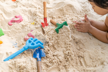 Fototapeta na wymiar A little girl playing plastic children toys in sandpit outdoor.