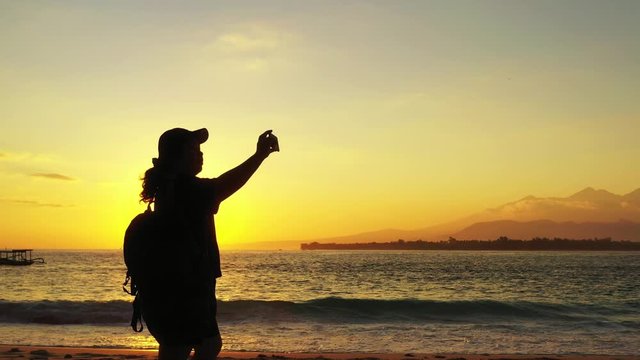 A tourist backpacker taking photos during a beautiful orange sunset on a tropical beach island