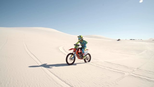 Professional dirt bike rider riding on the desert sand. Racer doing wheelie on motocross bike in desert.