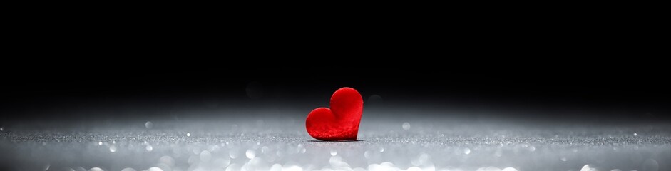 Tiny red heart in silver glittering spotlight with blank black space for text.