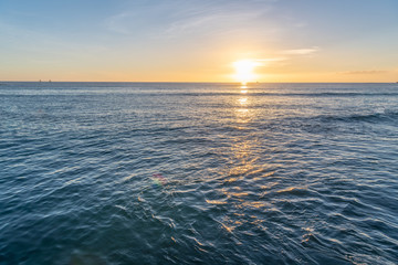 Beautiful yellow sunset over a deep blue ocean, with a sailboat in the distance, at Waikiki Beach...