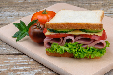 A delicious sandwich with sausage, cheese, tomatoes and lettuce.