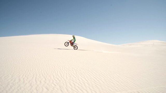 Dirt biker pulling a wheelie on the sand dunes. Motor cycle rider riding his bike across desert.