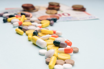 Path of tablets of different sizes and colored capsules leads to paper banknotes and coins. Concept of high profitability from production and sale of medicines, vitamins, and dietary supplements