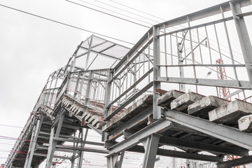 Fragment of staircase of pedestrian bridge over railway. Rusty metal floors. Lines of electrical wires are drawn against gray sky. Side view. Transport infrastructure