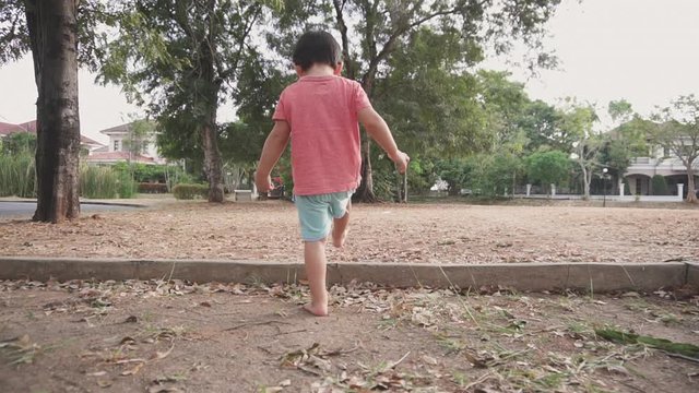 Two year old Asian toddler walking barefoot on the sand and dry leaves  at an outdoor park with a freedom and wild vibe