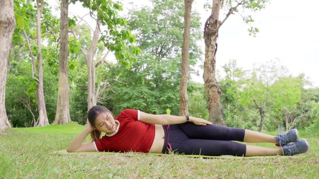 Young fit happy Asian woman, laying side way, working on her lef lifting routine during her morning exercise at a local park on an overcast day