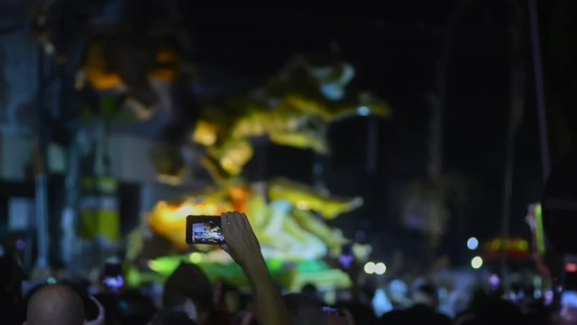 night festival with moving animal figure sillhouette. people hands holding mobile phones recording video, taking photo. crowd in dark. audience filming concert event