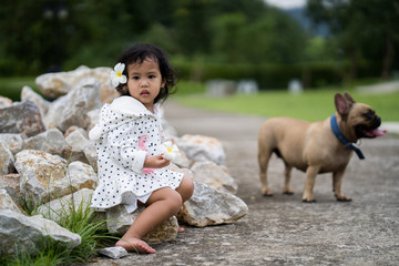 Cute little girl sitting at the rocks at park with her french bulldog.