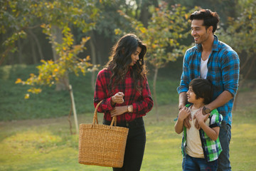 Happy young couple and their child walking in garden with the woman carrying a basket.