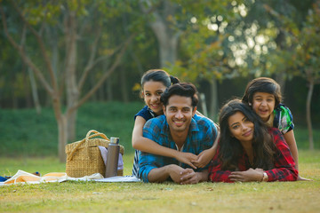 Happy man and woman on a picnic lying down in garden beside a picnic basket and their children lying on their backs.