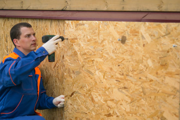 a worker in a blue uniform covers the lower part of the house with wooden boards. there is a place for an inscription on the right