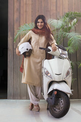 Smiling young woman in traditional dress posing with a scooter holding a helmet. © IndiaPix