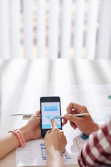 Hands of business people pointing at smartphone screen with financial chart and analzying sales and revenue