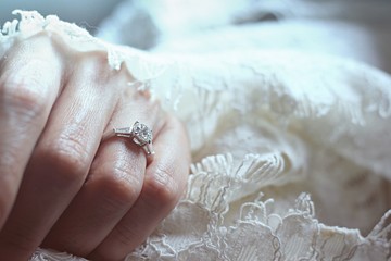 Close up Bride hand with beautiful diamond ring on white dress in warm light background.