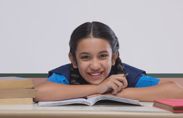 Portrait of school girl leaning on table while studying in classroom