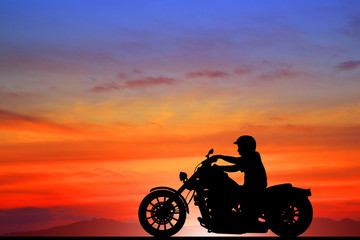 Plakat Silhouette biker with his motorbike beside the natural lake and beautiful sunset sky.