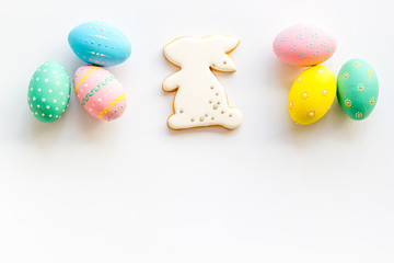 Obraz premium Easter symbols. Painted eggs and bunny gingerbread on white desk top-down frame copy space