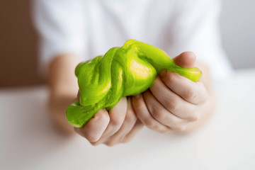 Children's hands hold a green slime and squeeze it. Focus on Slime