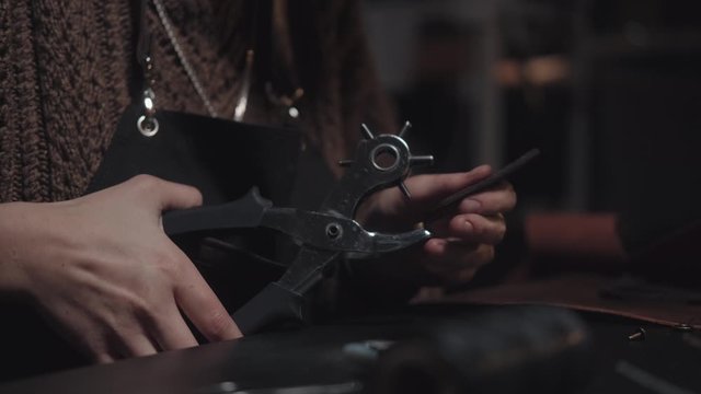 Close-up of the hands of a master tanner at work: processing leather with a special tool, a roller marker (copier) for marking. Handwork, craft business. Dark background, no people in the frame