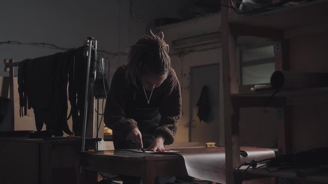A modern independent woman has own business: tanner with dreadlocks works in an art studio makes a leather product. General plan. Handmade, craft, hobby concept.