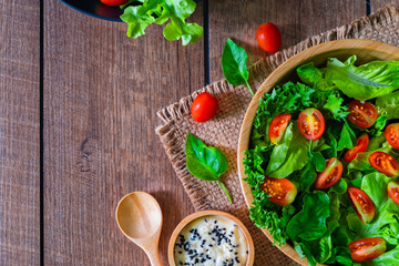 Fresh green vegetable salad. above of cherry tomato, onion, spinach and lettuce in wooden bowl with spoon, salad sesame dressing. Home made, Diet food for tasty and healthy meal. Top view, copy space.