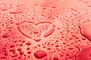 Heart made of water drops on a glass. The symbol of love and passion is drawn by hand. Wet red surface with condensation and raindrops. Background with copy space for a romantic greeting card.