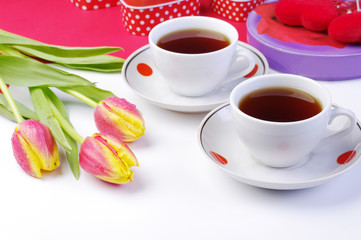 Obraz premium Tea for two. Two cups of tea and a bouquet of tulips on a table with a white tablecloth.