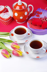 Tea for two. Two cups of tea, a bouquet of tulips, a porcelain teapot, gifts on a table with a white tablecloth.