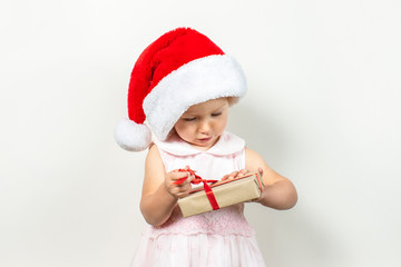 Little child in a hat of Santa Claus holds a gift on a light background. Banner. Gifts concept for christmas and winter holidays, happy family