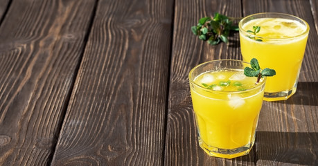 Two glass wiht orange juice wiht leaf mint and pices of ice on the dark wood board. Soft focus,...
