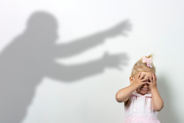 Fototapeta na wymiar Little child covers his face with his hands on a light background with the shadow of an attacking man. Concept of fear, fear, domestic violence, the game of locks