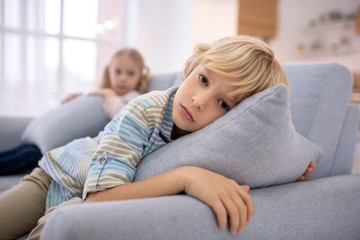 Blond cute boy with a pillow in his hands looking sad