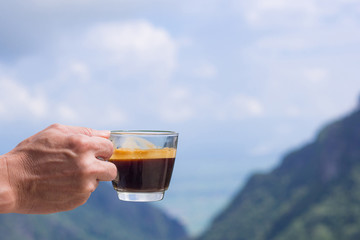 Close-up of a man hand holding a coffee cup with beautiful scenery view of mountains. Morning coffee feeling happy and freedom. Space for text