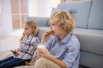 Boy eating biscuit and drinking milk, girl holding remote control