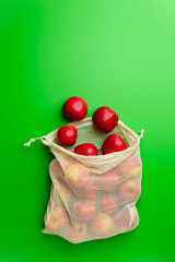 Grocery cotton net bag with red apples on a green background. Flat lay, copy space. Zero waste and no plastic concept.