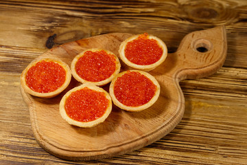 Tartlets with red caviar on a wooden table
