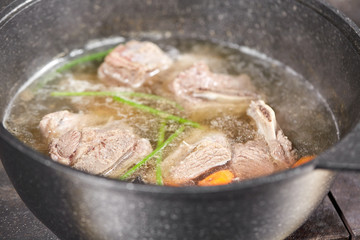Traditional beef broth with vegetable, bones and ingredients in pot, cooking recipe. Soup in a cooking pot with ladle on dark stone background. Top view