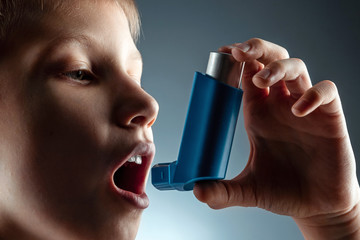 Portrait of a boy using an asthma inhaler to treat inflammatory diseases, shortness of breath. The concept of treatment for cough, allergies, respiratory tract disease. - obrazy, fototapety, plakaty