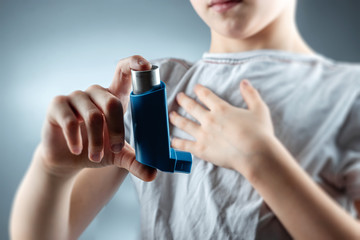 The boy holds an asthma inhaler in his hands to treat inflammatory diseases, shortness of breath. The concept of treatment for cough, allergies, respiratory tract disease. - obrazy, fototapety, plakaty