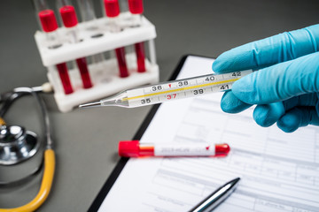 The doctor holds a thermometer in the background of a laboratory, test tubes with a blood test, a stethoscope