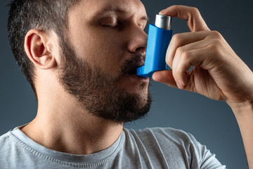 Portrait of a man with an asthma inhaler in his hands, an asthmatic attack. The concept of treatment of bronchial asthma, cough, allergies, dyspnea. - obrazy, fototapety, plakaty