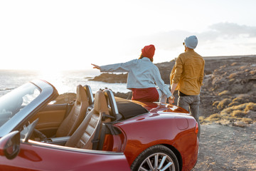 Couple enjoying beautiful views on the ocean, standing together near the car on the rocky coast....