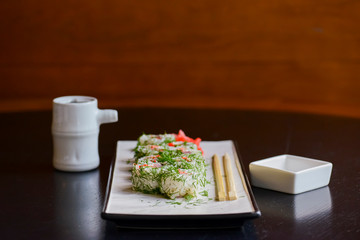 Salmon sushi rolls served on a white plate with ginger and wasabi and soy sauce in a restaurant table. Japanese cuisine.