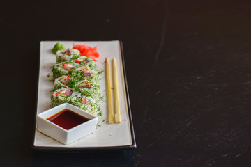 Fototapeta na wymiar Salmon sushi rolls served on a white plate with ginger and wasabi and soy sauce in a restaurant table. Japanese cuisine.